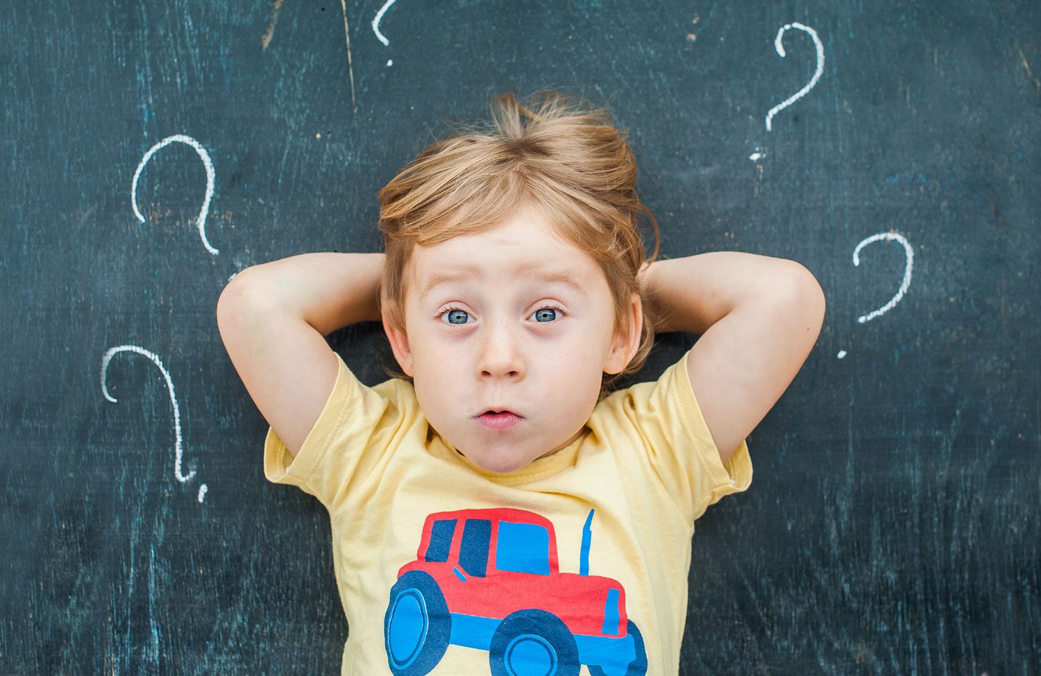 curious child leaning against chalkboard with question marks written on board