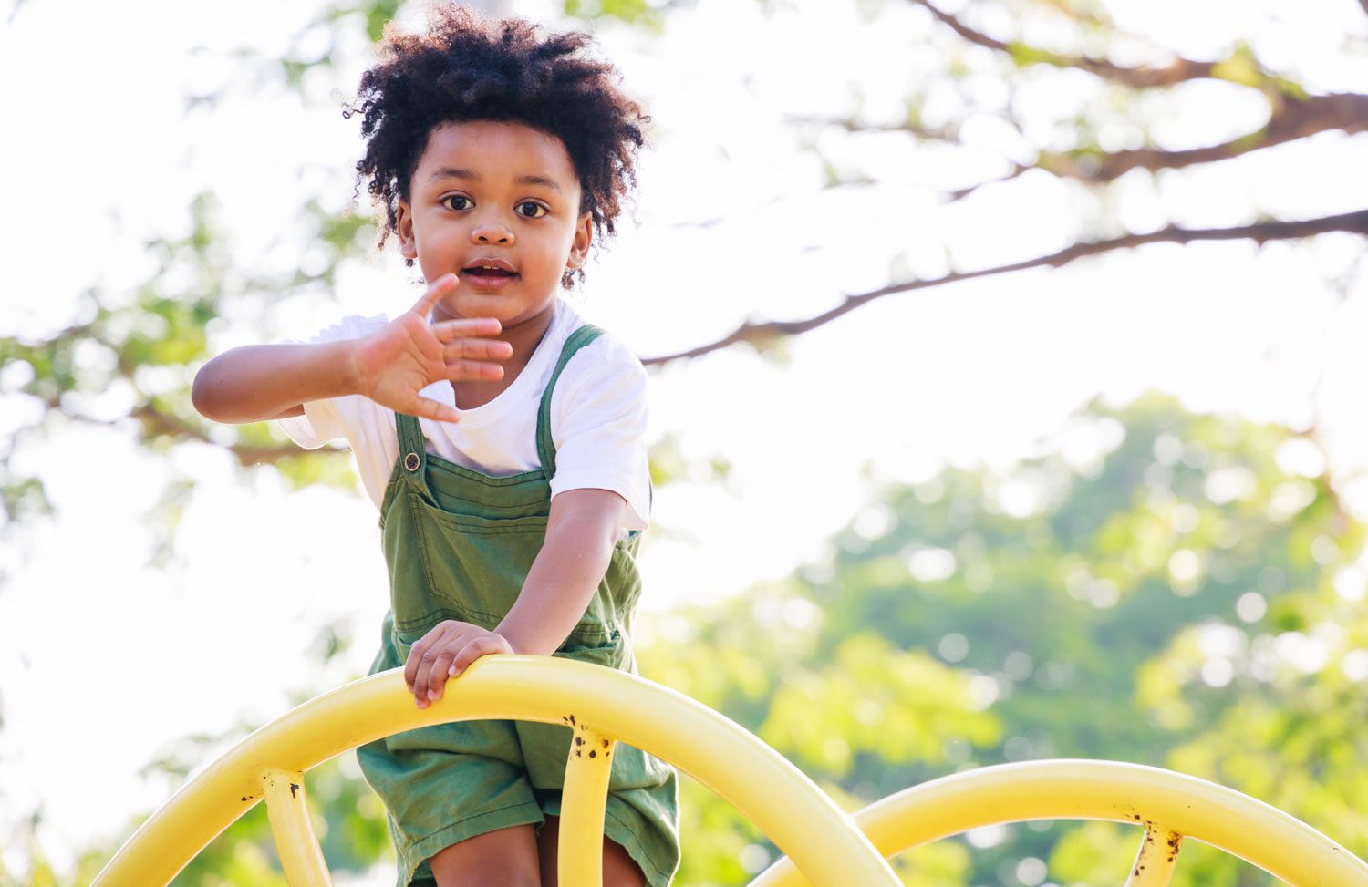 child climbing on playground equipment and waving