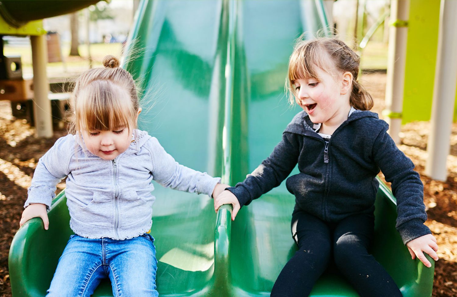 two children slide down a green playground slide