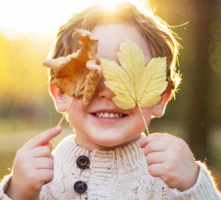 smiling child holding dry leaves in front of eyes