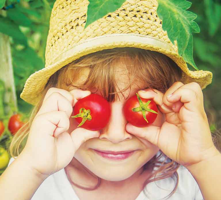 child holding small tomatoes in front of eyes