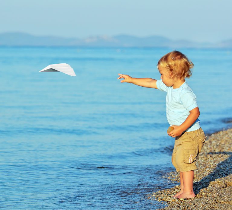 child throwing paper airplane from the shore of a body of water