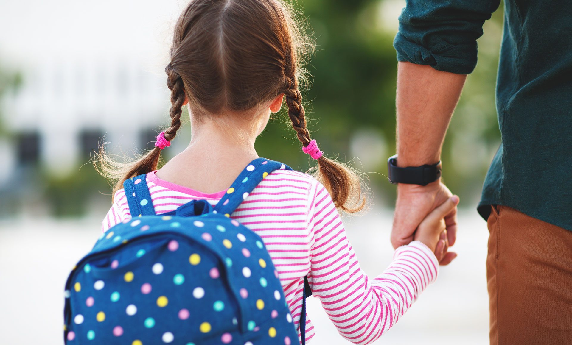 child wearing backpack holding adult's hand