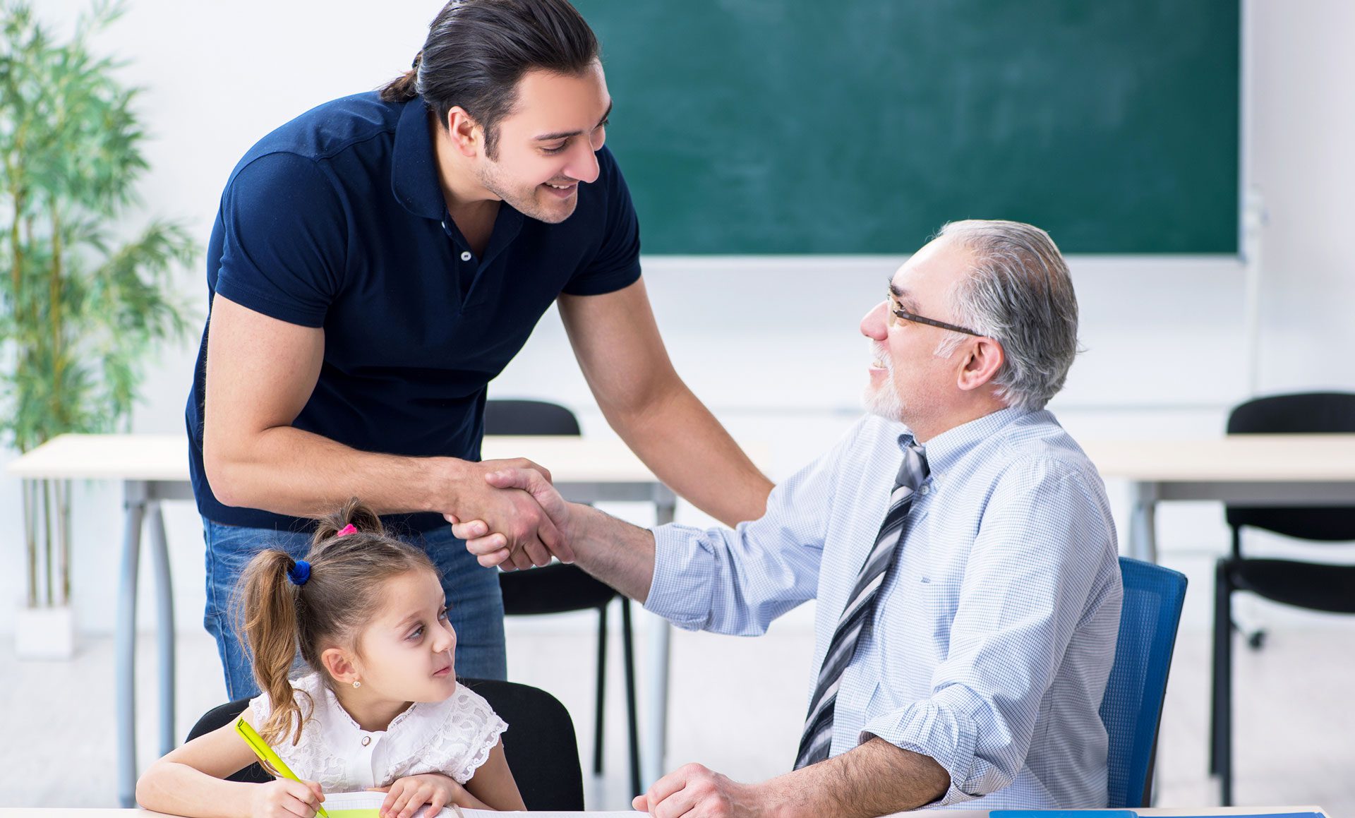 parent shakes hands with teacher while child looks on