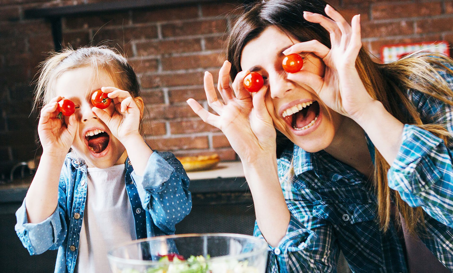 happy child and adult holding tomatoes in front of eyes while preparing a salad