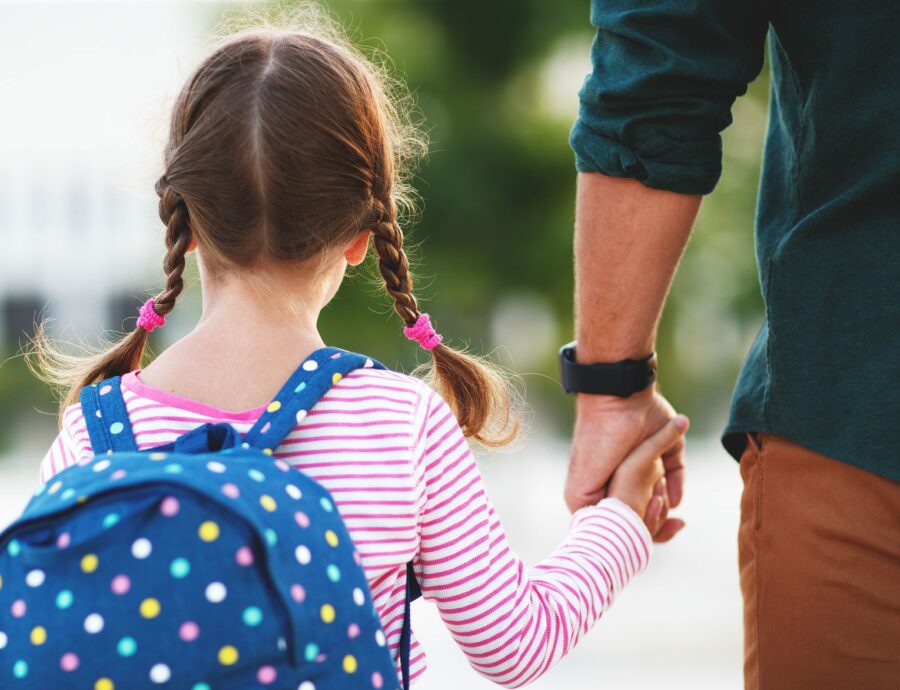 child with braided hair and backpack holding adult's hand