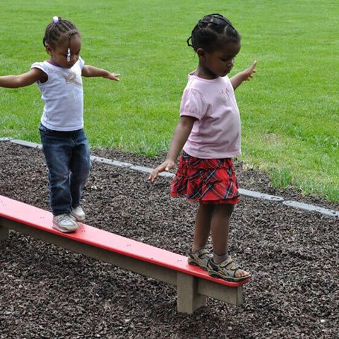 two children stand on a playground balance beam
