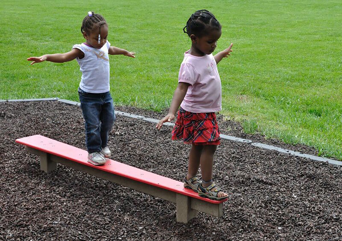 two children stand on a playground balance beam